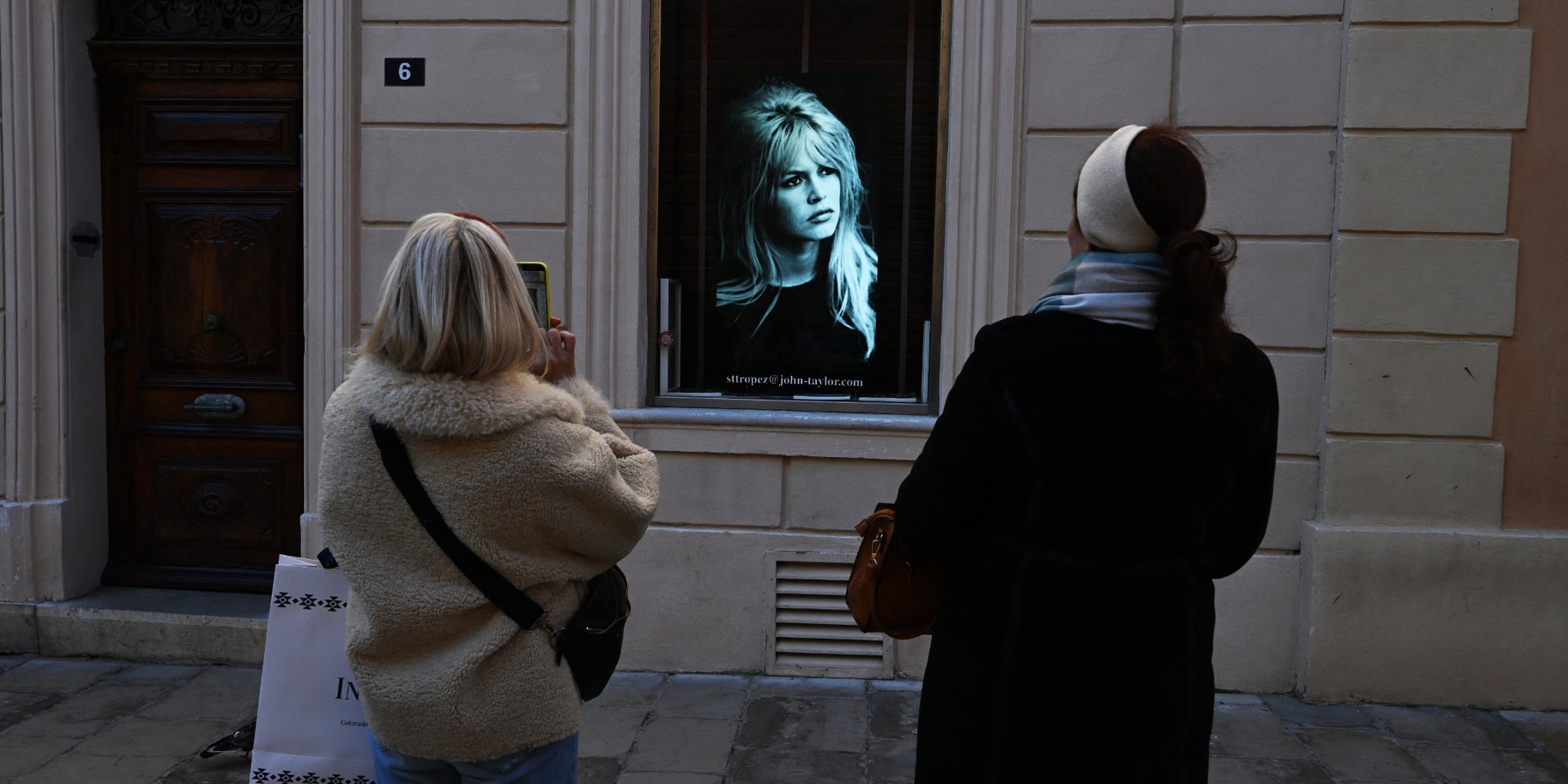 Deux passantes se tiennent face à un portrait de Brigitte Bardot affiché en vitrine, le jour des obsèques de la célèbre actrice française, le 7 janvier 2026 à Saint-Tropez.